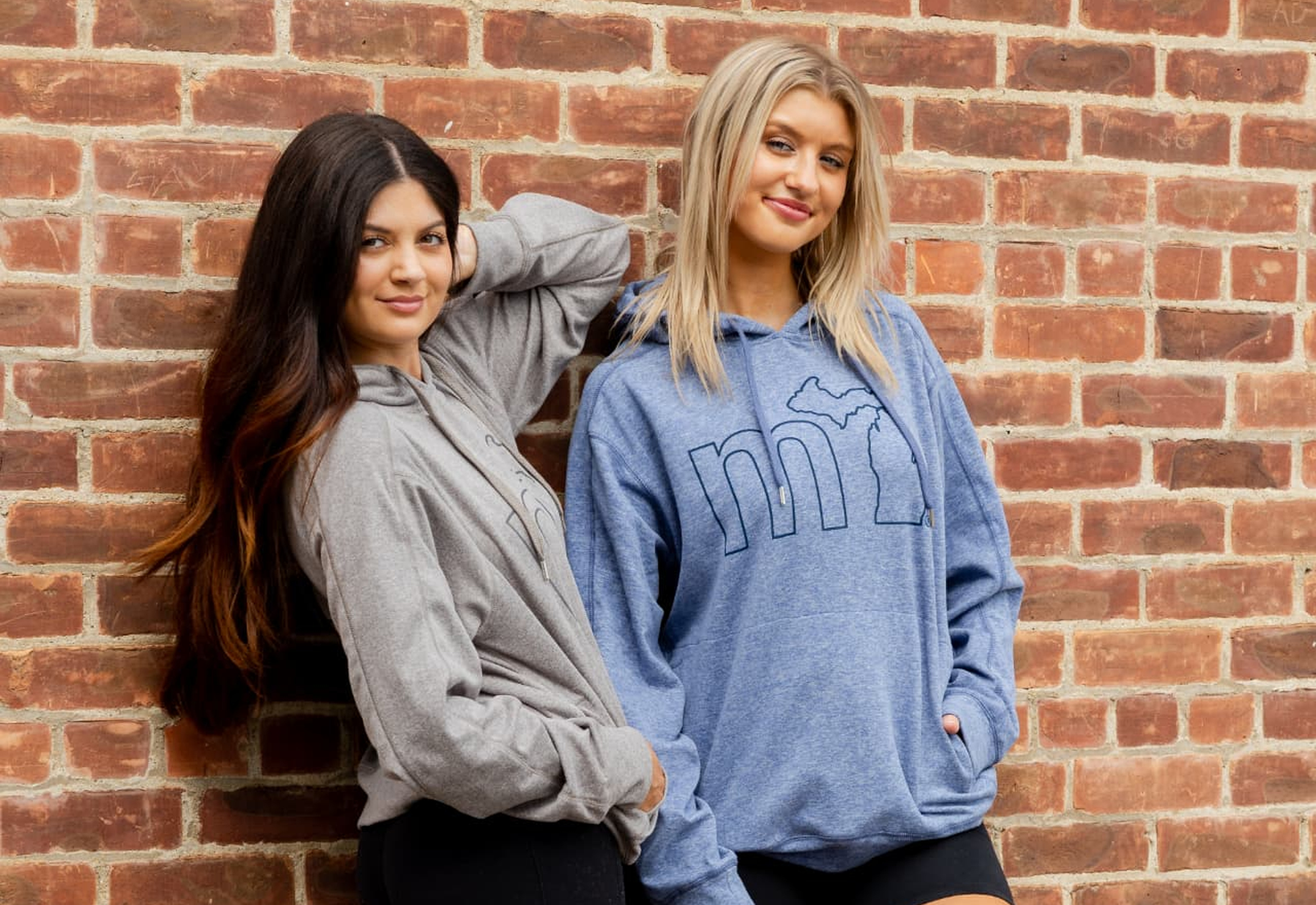 Two women wearing mi hoodies against a brick wall
