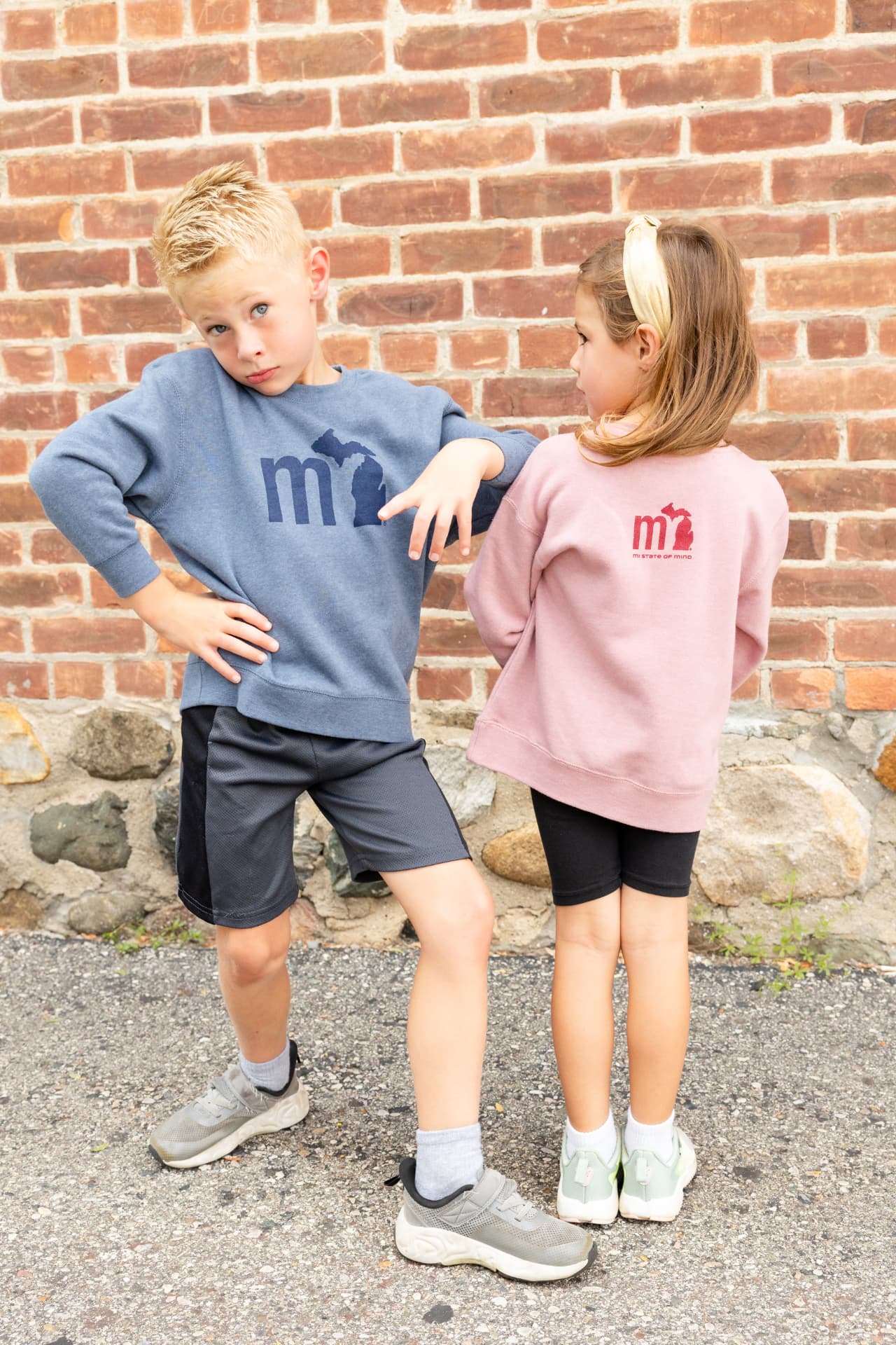 Two kids wearing mi crewneck sweatshirts against a brick wall